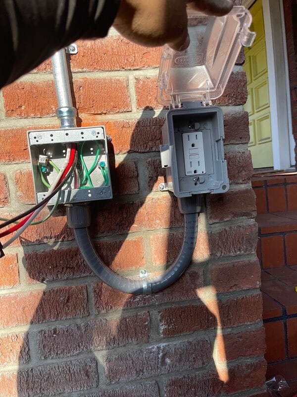 electrician holding open outdoor gfci cover next to open junction box