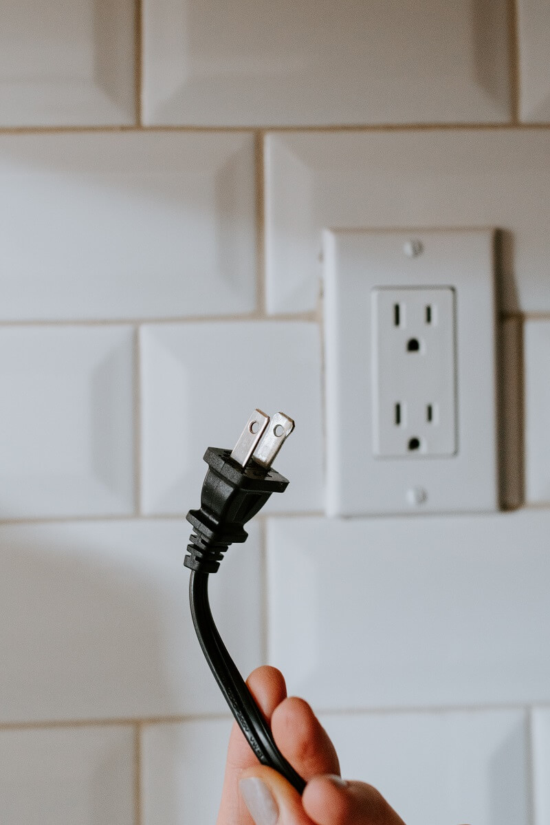 person holding up plug in front of outlet