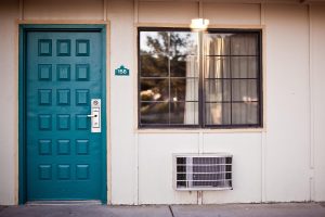 An exterior view of a motel room door and window with a through-the-wall air conditioning unit installed below the window.