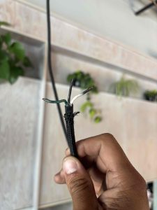 An electrician holding a stripped black fabric pendant light cable, showing exposed hot, neutral, and ground internal wires during a repair.
