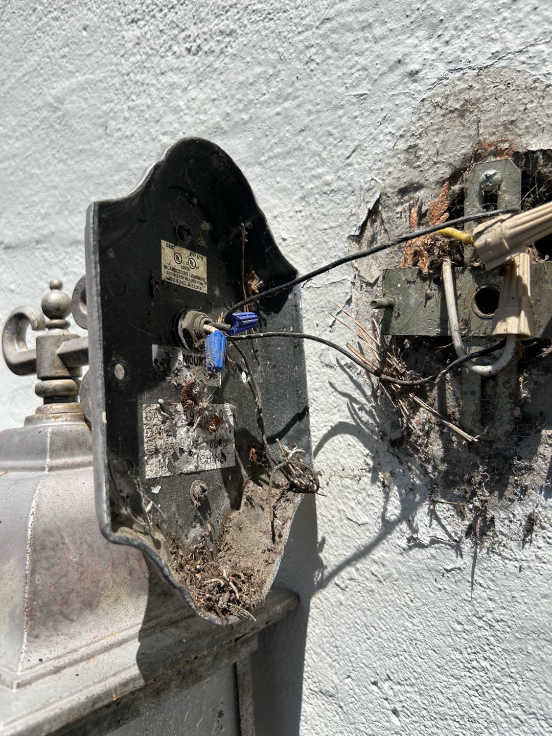 A detached exterior wall light fixture revealing exposed wiring connections during diagnostic troubleshooting.